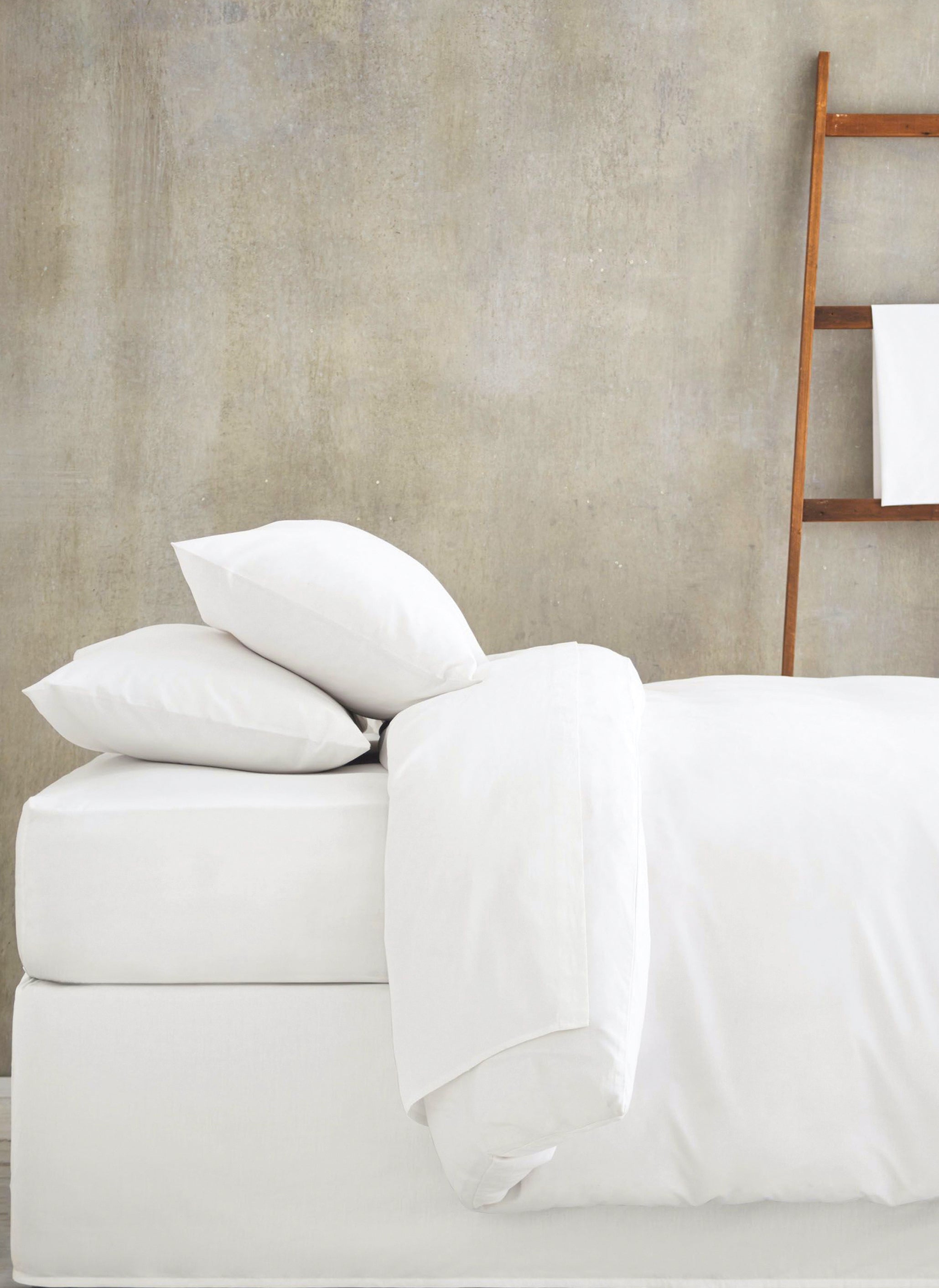 white bed linen on mattress and base set with white towel on towel ladder in background